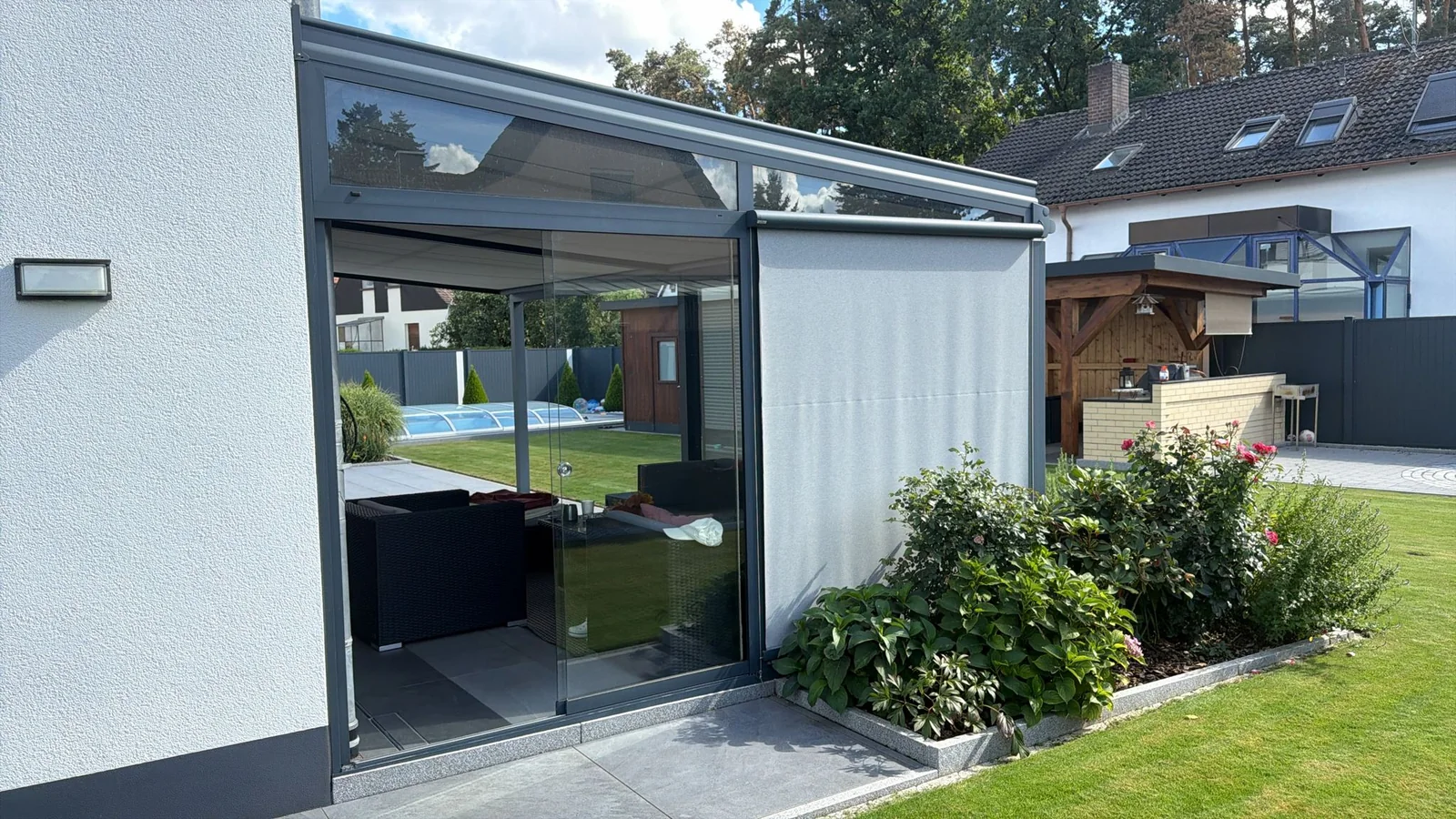 Reale Terrassenüberdachung mit seitlichem textilem Screen vor einer Glaswand